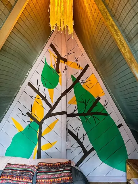 Pintura de árvore com galhos escuros e folhas verdes e amarelas no gable de madeira de um chalé