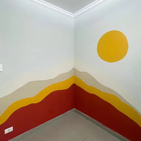 Mural de montanhas em camadas brancas, bege, amarela e vermelha com sol amarelo no canto da parede
