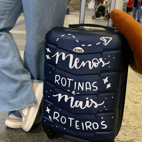 Mala de viagem azul pintada com letras brancas escritas “Menos rotinas e mais roteiros”