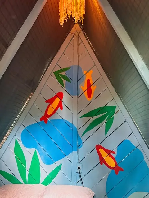 Pintura de peixes em azul, amarelo e vermelho com folhas verdes no gable de madeira de um chalé