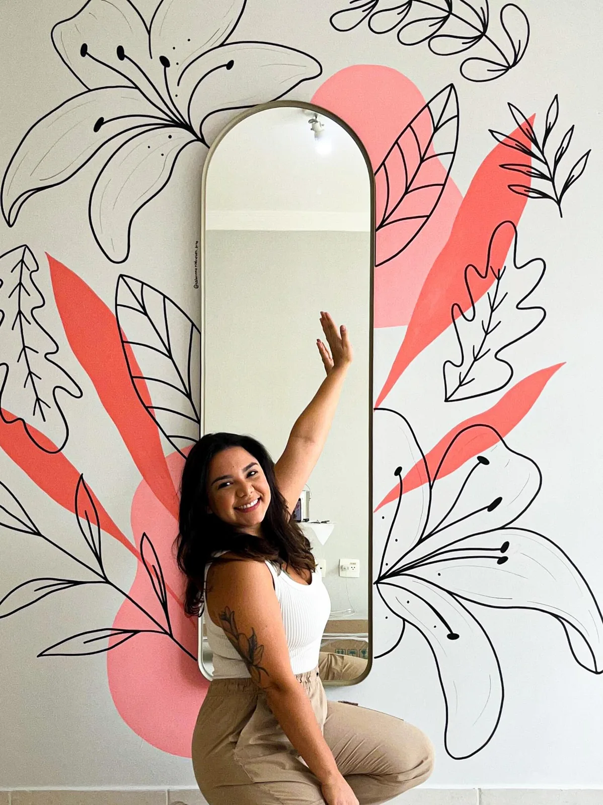 Sabrinna ao lado de sua pintura floral em coral ao redor de um espelho