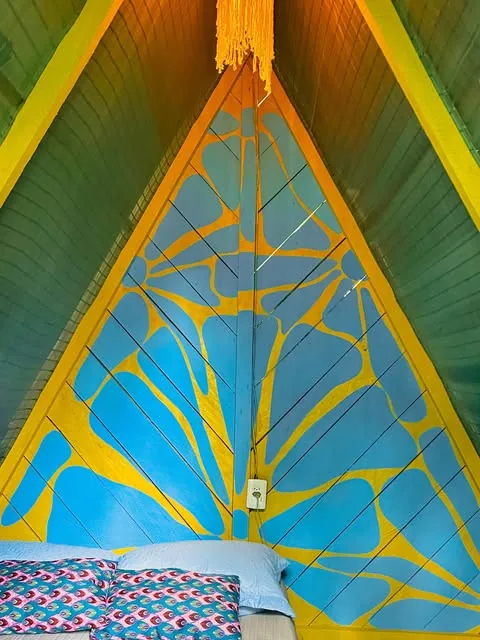 Pintura de formas orgânicas em azul e amarelo no gable de madeira de um chalé