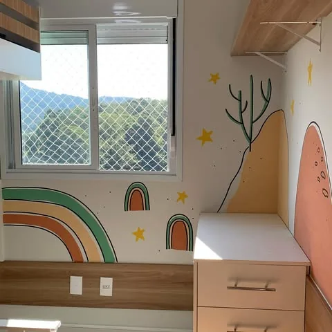 Mural com arco-íris em tons terrosos, estrelas, cacto e colina alaranjada em quarto com janela